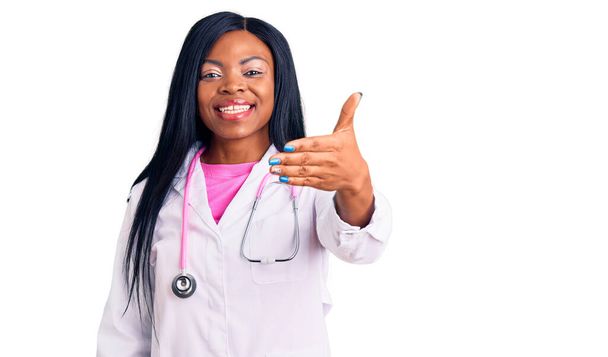 Młoda Afroamerykanka, nosząca stetoskop lekarski, uśmiechająca się, oferująca uścisk dłoni jako powitanie i powitanie. udany biznes.  - Zdjęcie, obraz