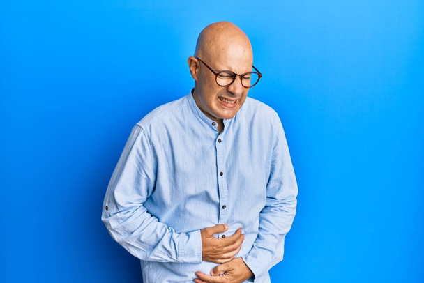 Middle age bald man wearing casual clothes and glasses with hand on stomach because nausea, painful disease feeling unwell. ache concept.  - Photo, Image