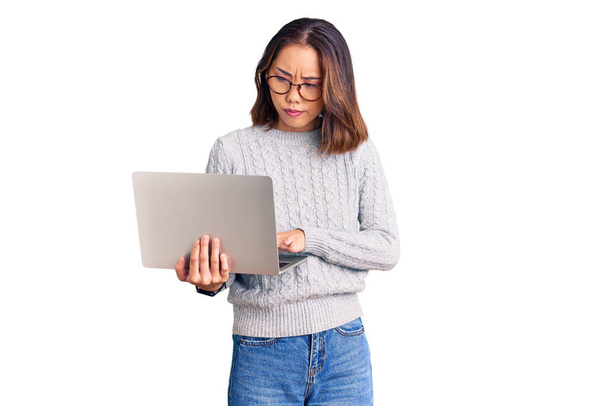 Young beautiful chinese girl wearing glasses holding laptop thinking attitude and sober expression looking self confident  - Foto, imagen