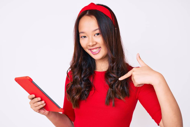 Молодая красивая китайская девушка держит тачпад указывая пальцем на один самодовольный счастливый и гордый  - Фото, изображение
