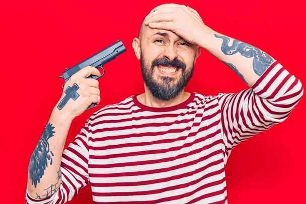 Молодой красивый мужчина, держащий пистолет напряжен и разочарован рукой на голове, удивлен и сердитый лицо  - Фото, изображение