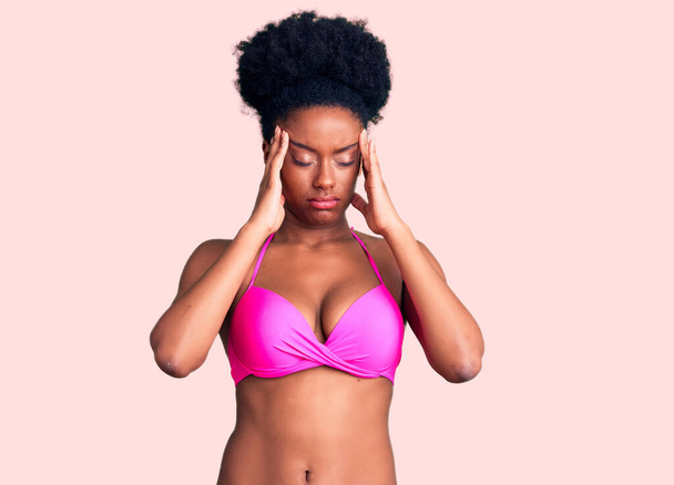 Giovane donna afroamericana in bikini che soffre di mal di testa disperato e stressato perché il dolore e l'emicrania. mani sulla testa.  - Foto, immagini