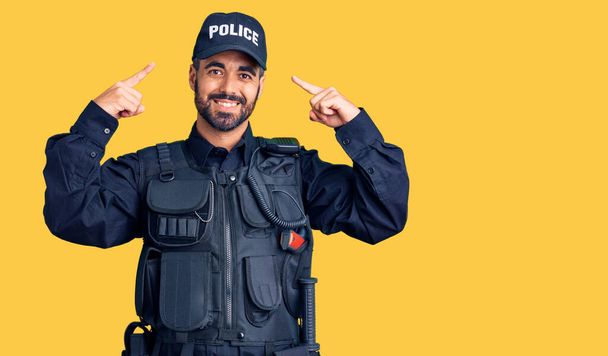 両手の指で頭を指して警察の制服を着て若いヒスパニック系の男,素晴らしいアイデアや考え,良い記憶  - 写真・画像