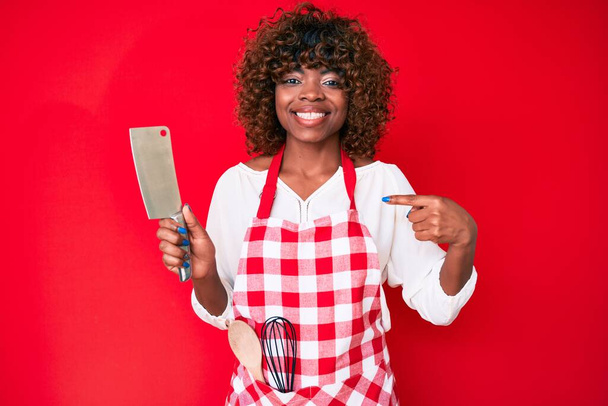 Молода афроамериканка, одягнена в куховарку фартух з ножем, вказує пальцем на усмішку щасливою і гордою.  - Фото, зображення