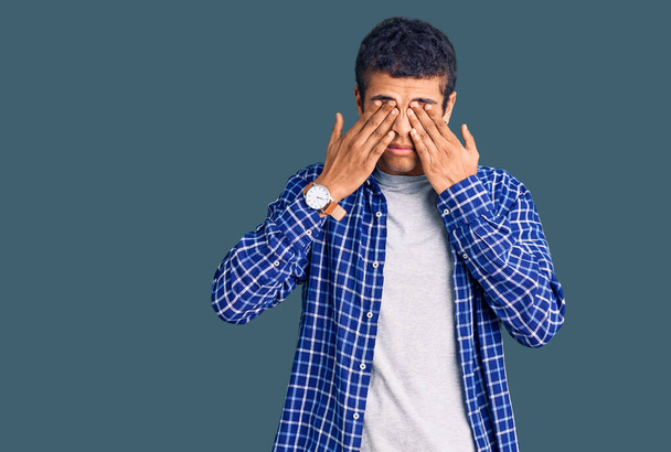 Hombre joven amerciano africano que usa ropa casual frotando los ojos para la fatiga y el dolor de cabeza, la expresión somnolienta y cansada. problema de visión  - Foto, imagen