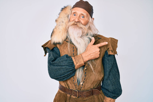 Старик с седыми волосами и длинной бородой в традиционном костюме викинга улыбается веселым указанием рукой и пальцем в сторону  - Фото, изображение