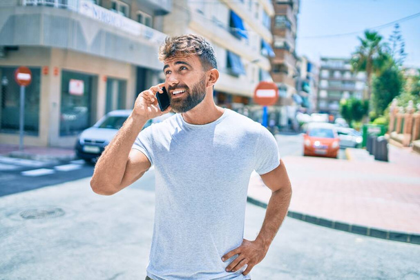 Fiatal spanyol férfi mosolyog boldog használ smartphone séta a cit - Fotó, kép