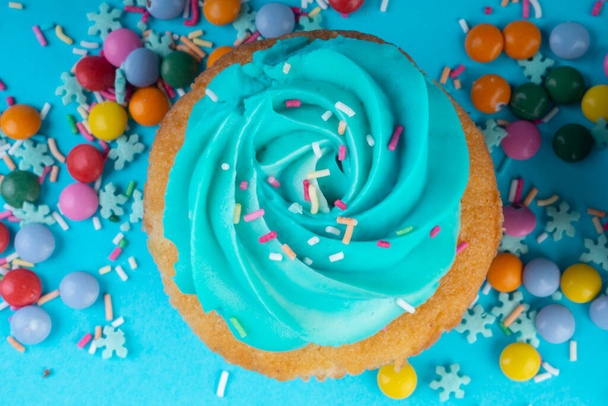 Cupcake kermavaahtoa sinisellä pohjalla, koristeltu sokeri lumihiutaleet, strösselit, värikäs karkkeja, valikoiva keskittyä - Valokuva, kuva