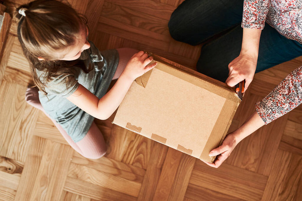 Woman unpacking a cardboard box parcel in room at home. Little girl waiting for opening a gift in package - Photo, image
