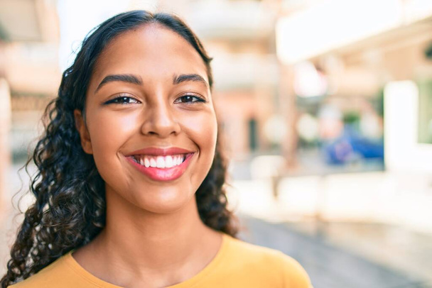 Νεαρή Αφρικάνα Αμερικανίδα χαμογελάει χαρούμενη περπατώντας στην πόλη. - Φωτογραφία, εικόνα