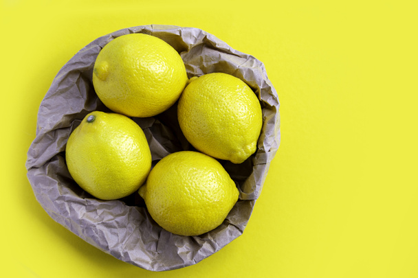 Concepto de embalaje ecológico. Cuatro limones maduros sobre fondo amarillo. Grupo de limón fresco en bolsa de papel de reciclaje. Lugar para texto, espacio de copia - Foto, imagen