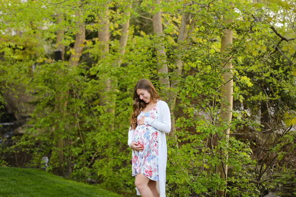 Young pregnant woman walking in forest and wearing dress. - Photo, Image
