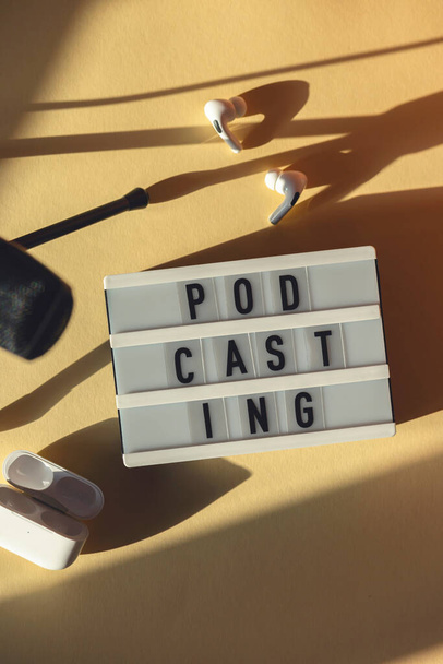 Podcasting betű mellett mikrofon és vezeték nélküli fejhallgató a munkahelyen kemény árnyékban - Fotó, kép