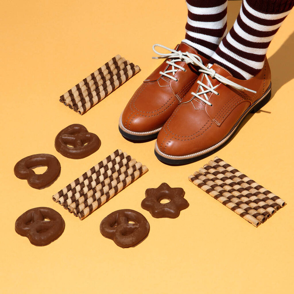 Leg in vintage striped socks and shoes in stylish isometric sweet cookies space. Minimal still life fashion food art. Chocolate lover. Holidays party time, winter christmas mood season - Foto, Imagem