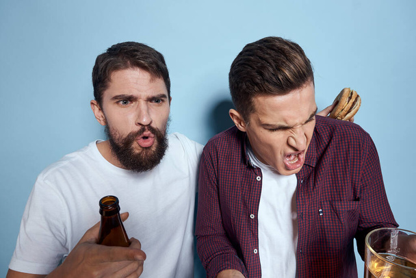 Δύο χαρούμενα μεθυσμένοι φίλοι πίνοντας μπύρα συναισθήματα τρόπο ζωής σε ένα μπλε φόντο - Φωτογραφία, εικόνα