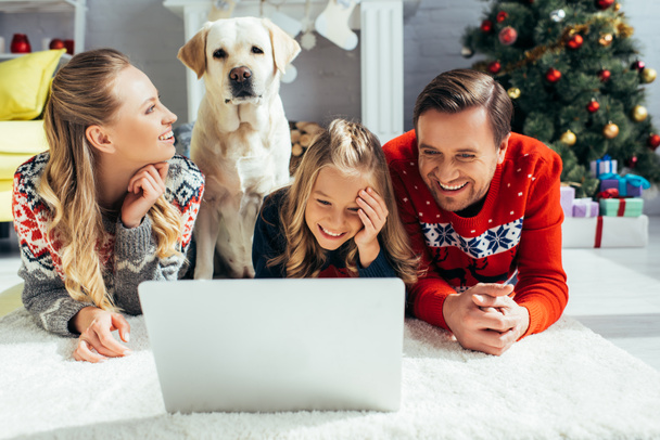 famiglia felice ridendo mentre guarda il film sul computer portatile vicino al cane a Natale  - Foto, immagini