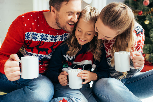 happy family in sweaters holding cups with drinks on christmas  - Фото, изображение