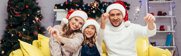 happy family in santa hats holding sparklers in decorated living room, banner - Photo, Image