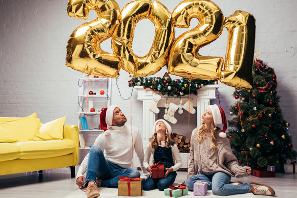 surprised family in santa hats sitting near presents and shiny balloons with 2021 numbers  - Фото, зображення