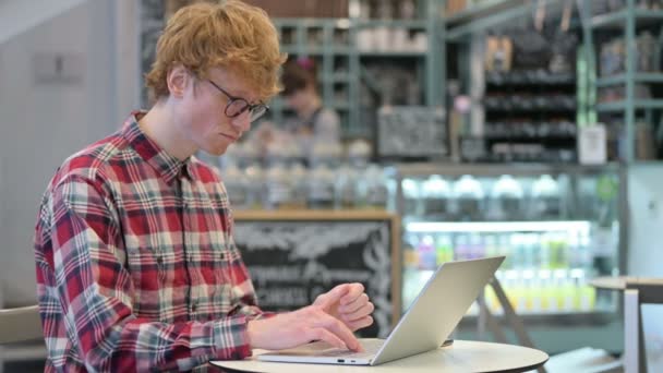 Молодой рыжий с ноутбуком мышление в кафе  - Кадры, видео