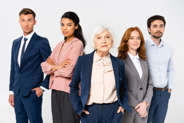 Senior businesswoman looking at camera near multicultural colleagues isolated on grey - Photo, Image