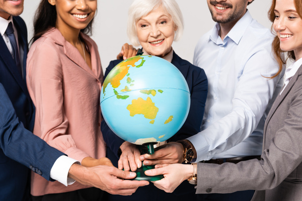 Globe in handen van glimlachende multi-etnische zakenmensen op wazige achtergrond geïsoleerd op grijs - Foto, afbeelding