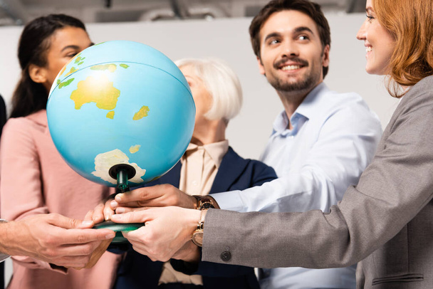 Глобус в руках улыбающихся мультиэтнических бизнесменов на размытом фоне  - Фото, изображение
