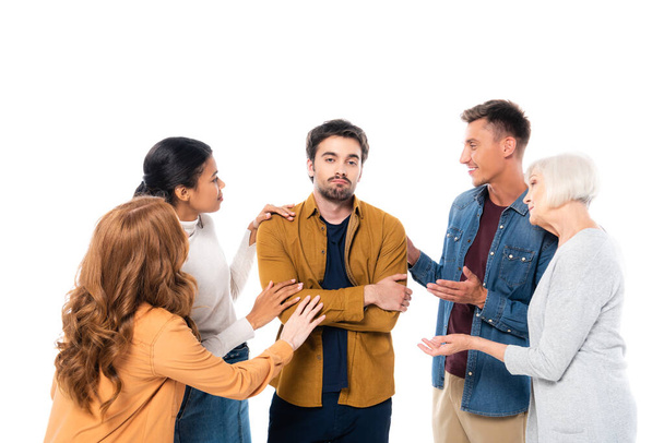 Triste homme aux bras croisés se tenant près d'amis multiethniques isolés sur blanc - Photo, image