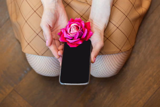 schöne rosa Blume und Smartphone mit schwarzem Bildschirm in Frauenhand, Kopierraum-Konzept Hintergrund - Foto, Bild