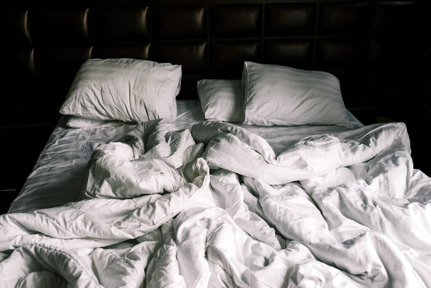 Niepościelone podwójne puste łóżko z białą pościelą. Pościel i poduszki w apartamencie lub hotelu po nocy snu. Łóżko było brudne i niepościelone. Zgniatany koc w sypialni. - Zdjęcie, obraz