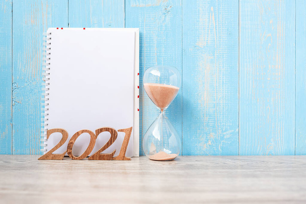 2021 Frohes Neues Jahr mit leerem Notizbuch, Sanduhr und Holzzahl. Countdown, Neuanfang, Resolution, Ziele, Plan, Handlungs- und Missionskonzept - Foto, Bild
