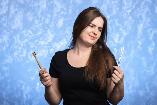 a young woman holds two toothbrushes in her hands: a plastic one and a bamboo one. look disdainfully towards the plastic. oral hygiene. - Foto, Imagem