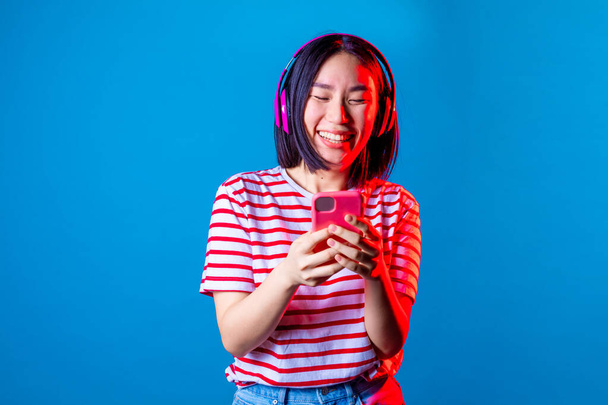 Junge schöne asiatische Frau per SMS auf blauem Hintergrund - Isolierte asiatische junge Frau mit Smartphone lächelnd Studioaufnahme - Soziales Netzwerk, Technologie, Diversitätskonzept - Foto, Bild