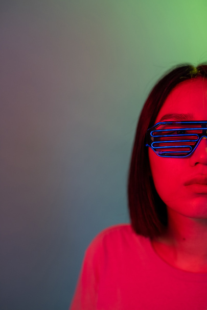 Jonge vrouw met koptelefoon en futuristische led-bril op groene achtergrond - Isolated woman clubbing silent disco wearing neon glasses and headphone - party, future, technology concept  - Foto, afbeelding