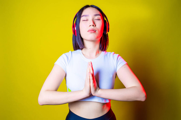 Asiatic young woman listening music meditating on yellow background - Female asiatic isolated relaxing doing yoga listening music -  harmony, calming, spirituality concept - Фото, изображение