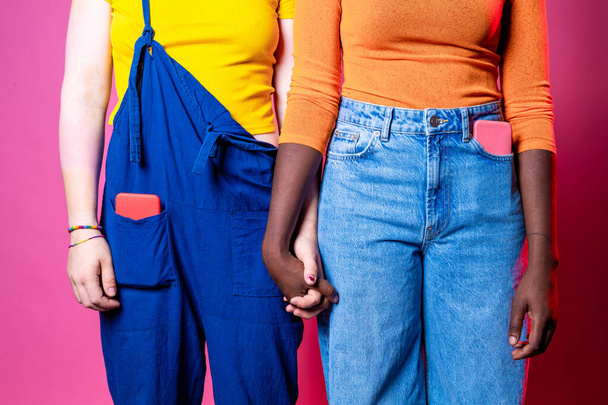 Diverse black and caucasian women holding hands - Two multi-ethnic women standing hand in hand against racism over pink background - diversity, inclusion, femininity concept - Foto, afbeelding