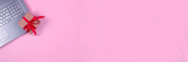 Баннер с видом сверху на ноутбук компьютер, настоящее поле с красным бантом на пастельно-розовом фоне с копирайтом для вашего текста. Seasonal sale, black friday and cyber monday concept, online shopping - Фото, изображение