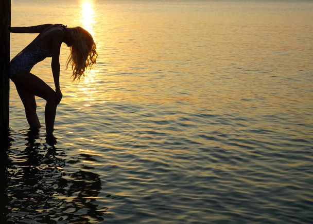 silhouette of  woman standing on seashore. sunlight. girl enjoy sunny sunset. Blonde long hair. - Foto, afbeelding