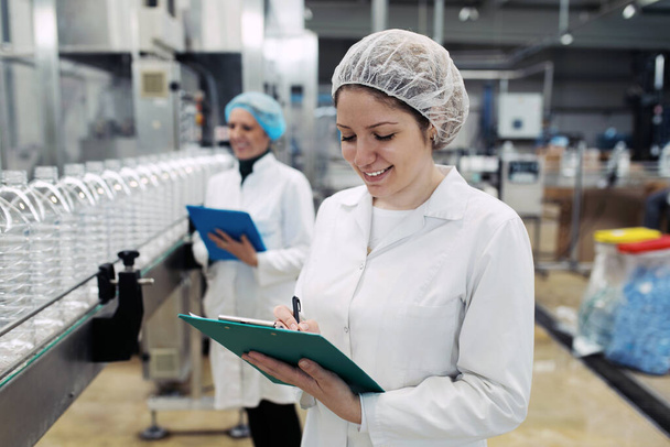 Kobiety pracujące w fabryce butelkowania sprawdzają butelki wody przed wysyłką. Kontrola jakości inspekcji.  - Zdjęcie, obraz