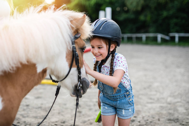Χαριτωμένο κοριτσάκι απολαμβάνει με άλογο πόνυ σε εξωτερικούς χώρους στο ράντσο. - Φωτογραφία, εικόνα