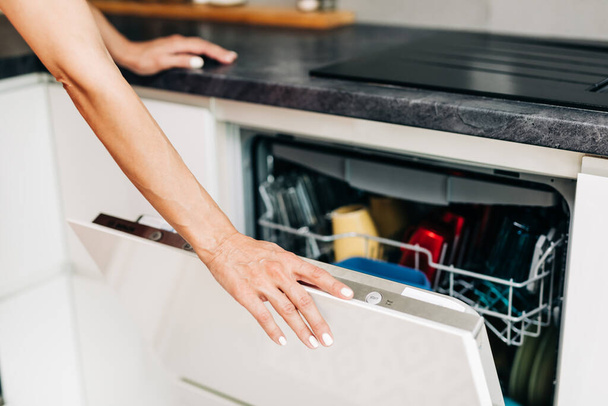 Main de femme avec un lave-vaisselle ouvert rempli de vaisselle propre - Photo, image