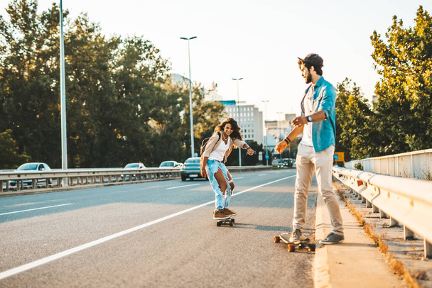 Beautiful young couple enjoying skateboarding on city street. - 写真・画像