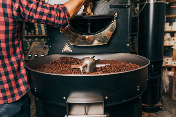 Les mains de l'homme tenant des grains de café aromatiques fraîchement torréfiés sur une machine de torréfaction de café moderne. - Photo, image