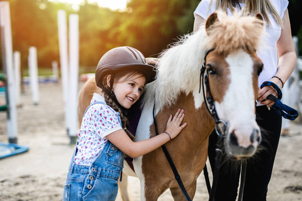 Cute little girl and her older sister enjoying with pony horse outdoors at ranch. - Photo, Image