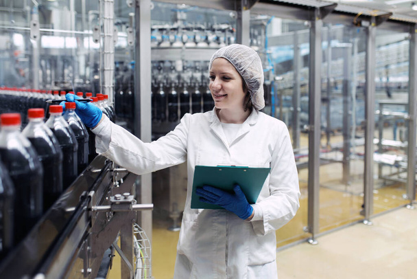 Молодая счастливая работница на заводе по розливу соков проверяет бутылки перед отправкой. Контроль качества.  - Фото, изображение
