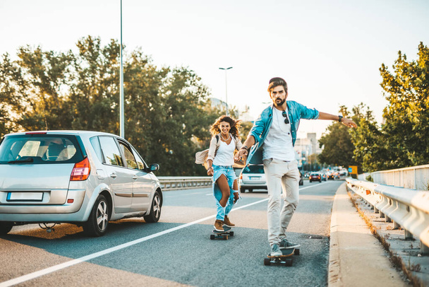 Beautiful young couple enjoying skateboarding on city street. - Foto, imagen