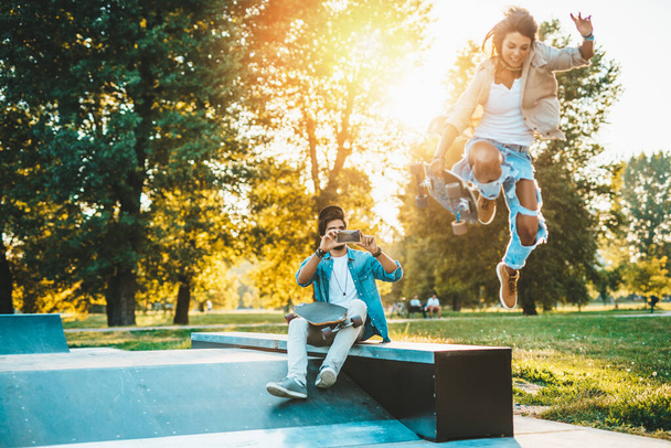Beautiful young couple enjoying outdoors adn taking photos in city skateborading park - Foto, afbeelding