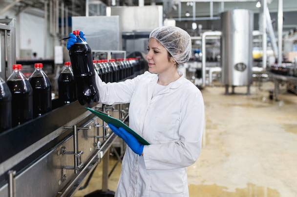 Молодая счастливая работница на заводе по розливу соков проверяет бутылки перед отправкой. Контроль качества.  - Фото, изображение