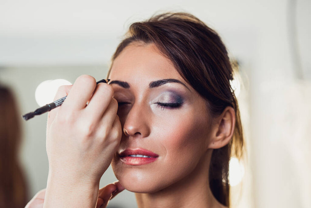 Make-up kunstenaar doen professionele make-up van mooie jonge vrouw - Foto, afbeelding