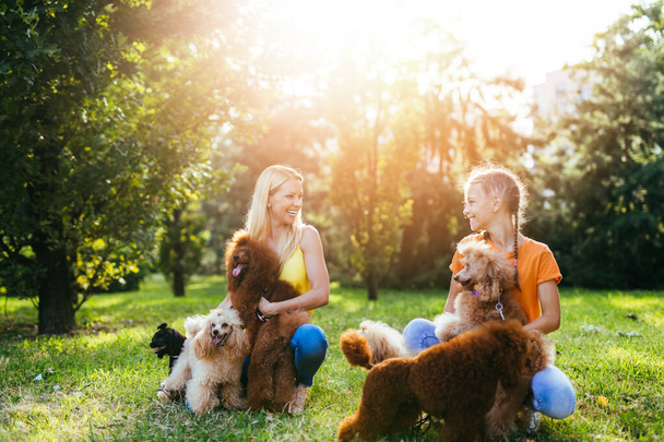 Mother and daughter enjoying together with their poodles in park. - Photo, Image